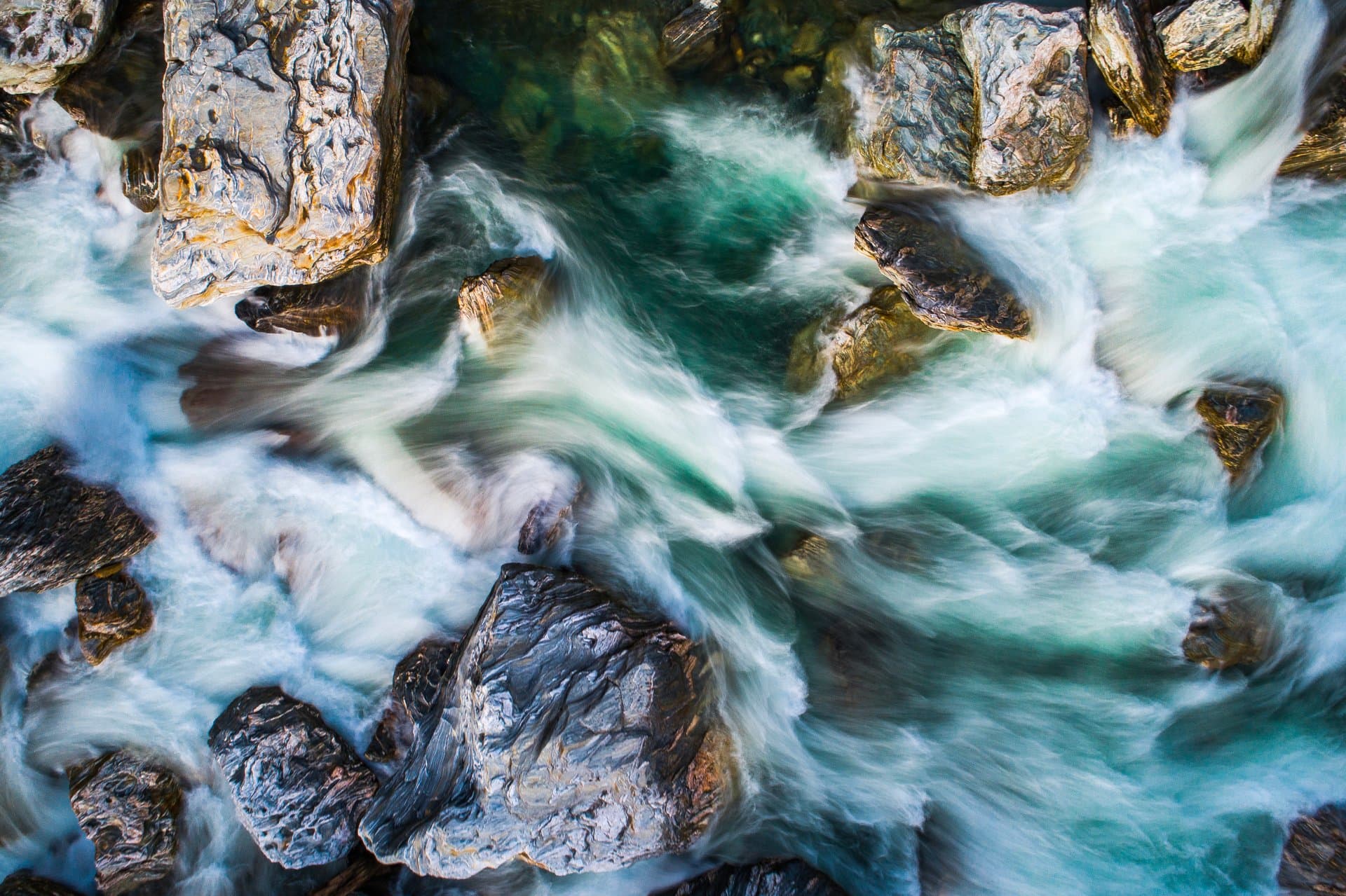 Aerial view of clear turquoise water cascading and swirling around rugged rocks in a pristine mountain headwater stream.