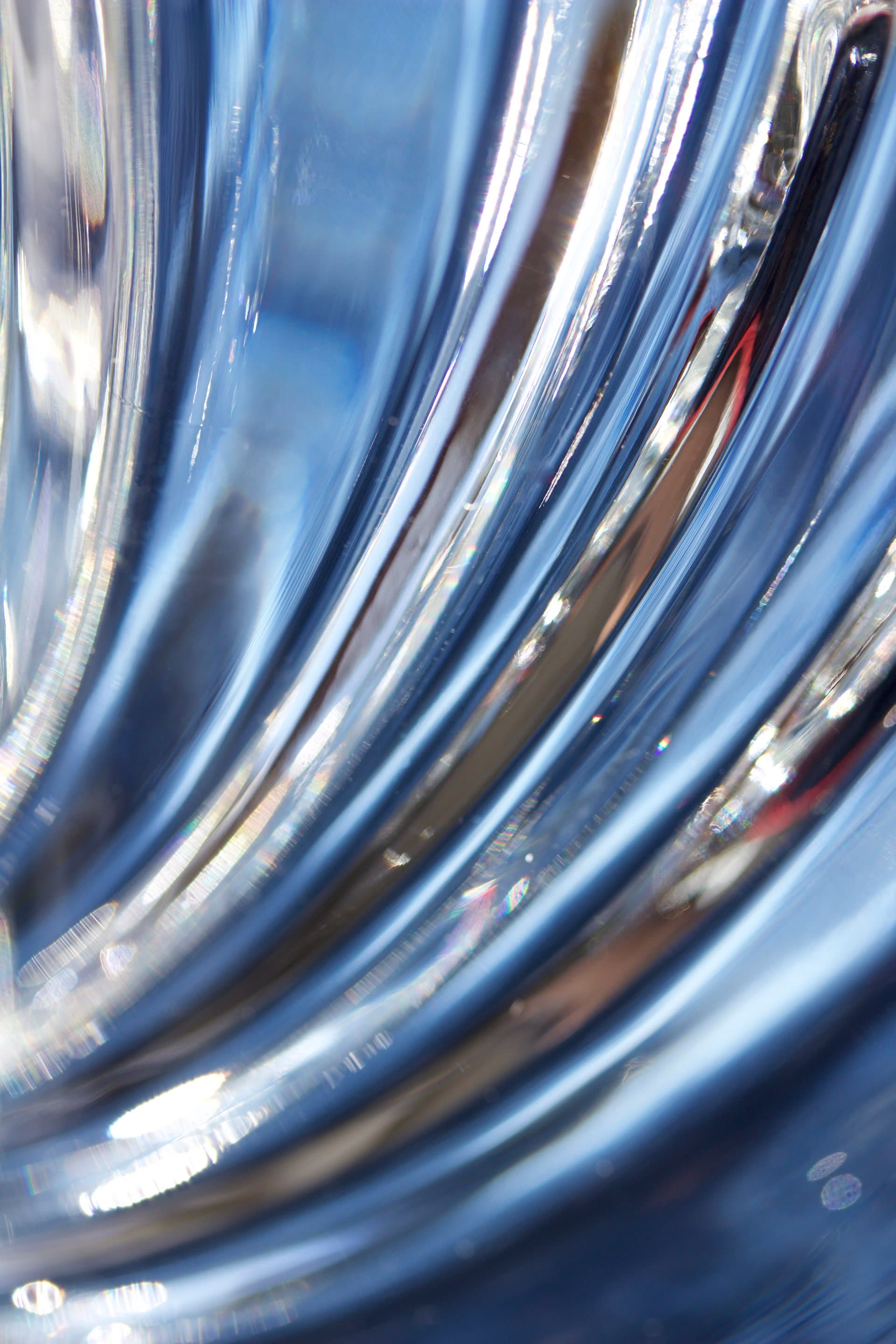 Close-up abstract image of flowing blue crystal glass with reflective curves and light refractions, evoking purity and clarity in healthcare.